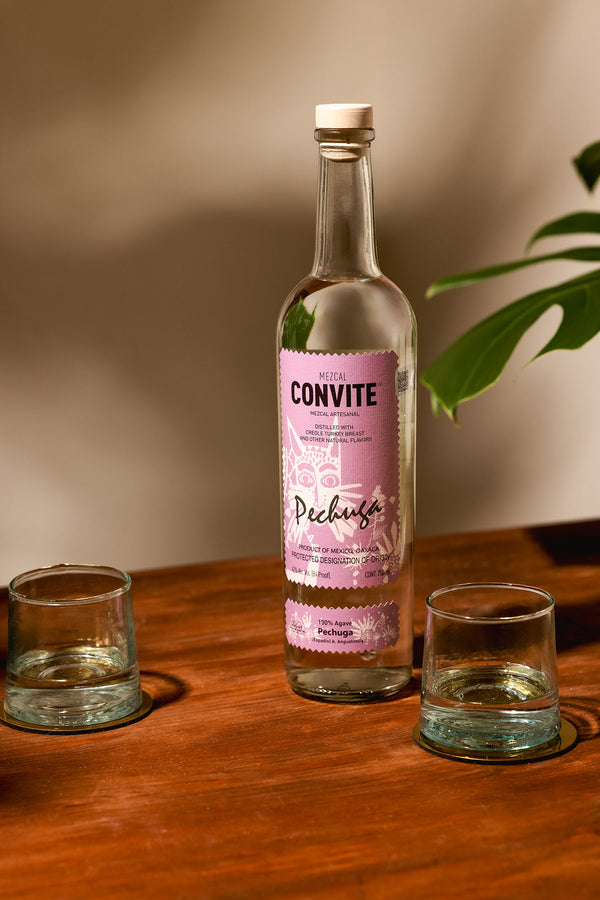 A bottle of Pechuga on a wood table with two glasses.